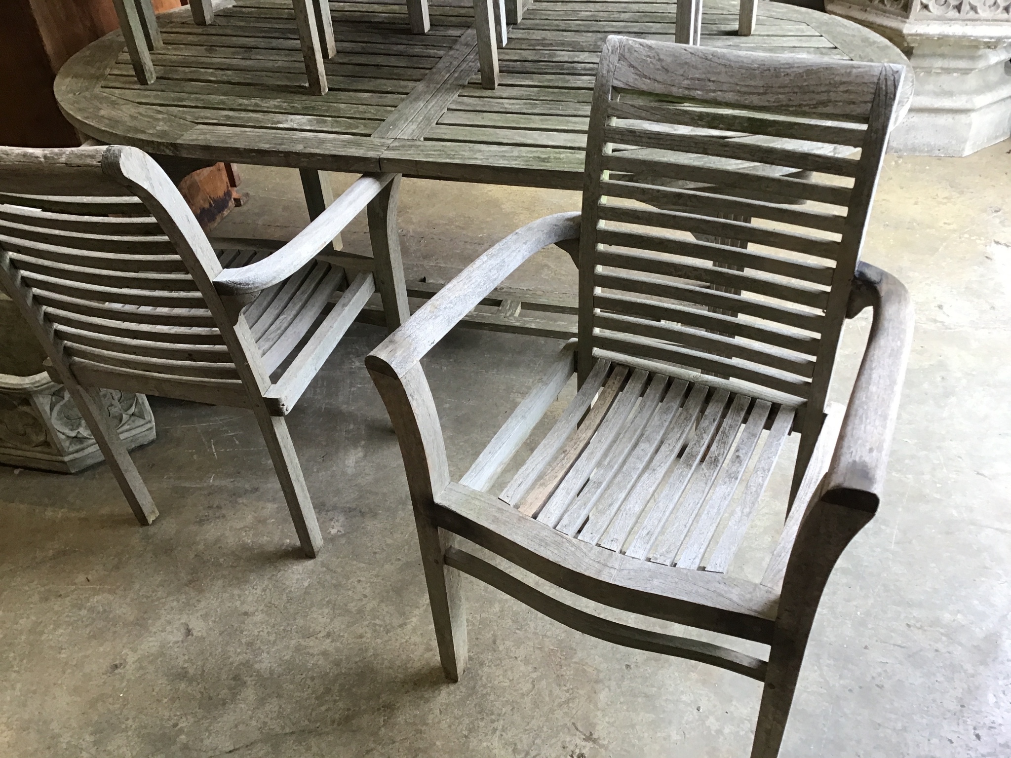 A weathered teak oval extending garden table, 242 cm extended, width 102 cm, height 73 cm and six stacking elbow chairs.